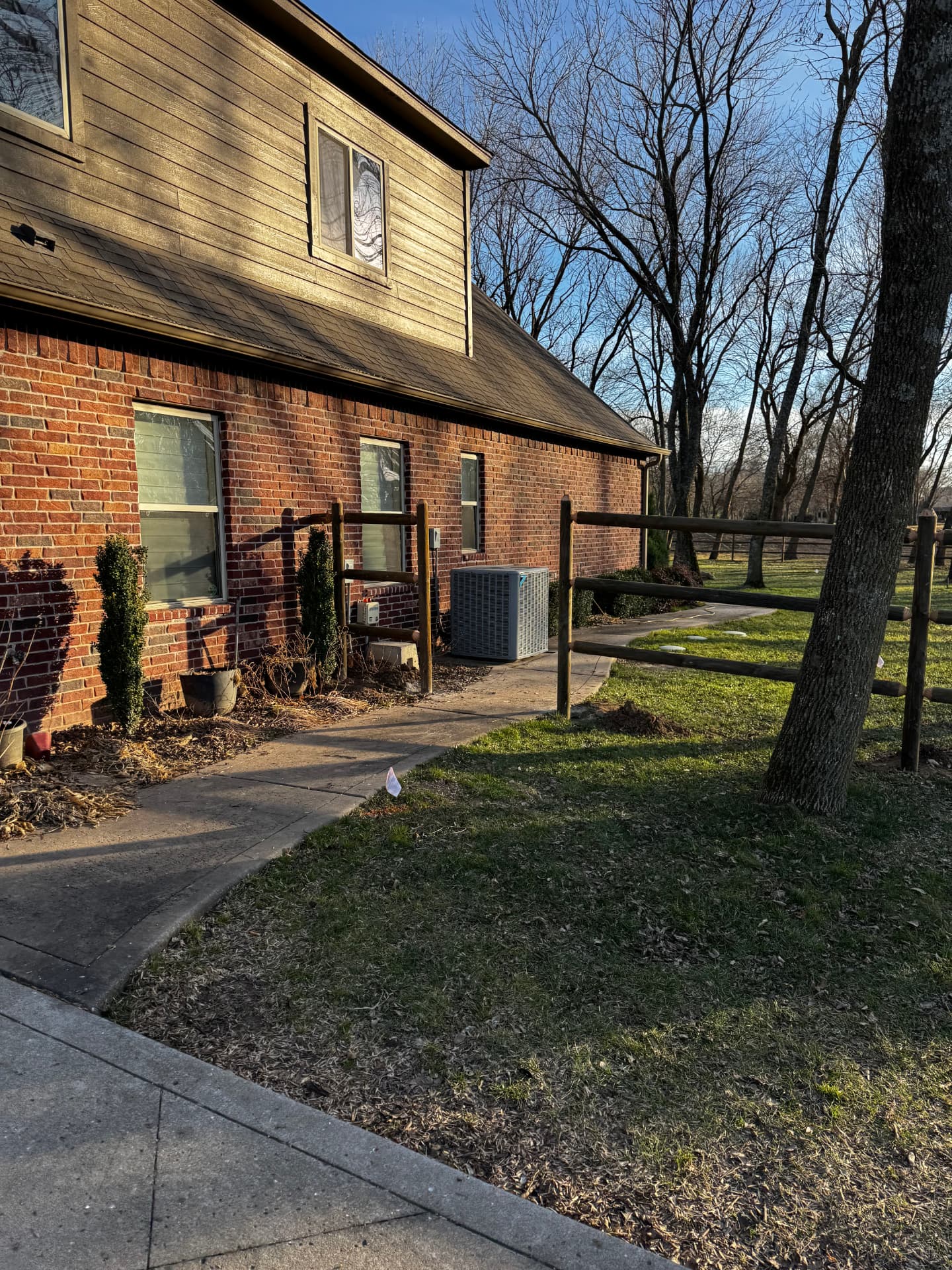 Open round rail fence entrance beside a brick home