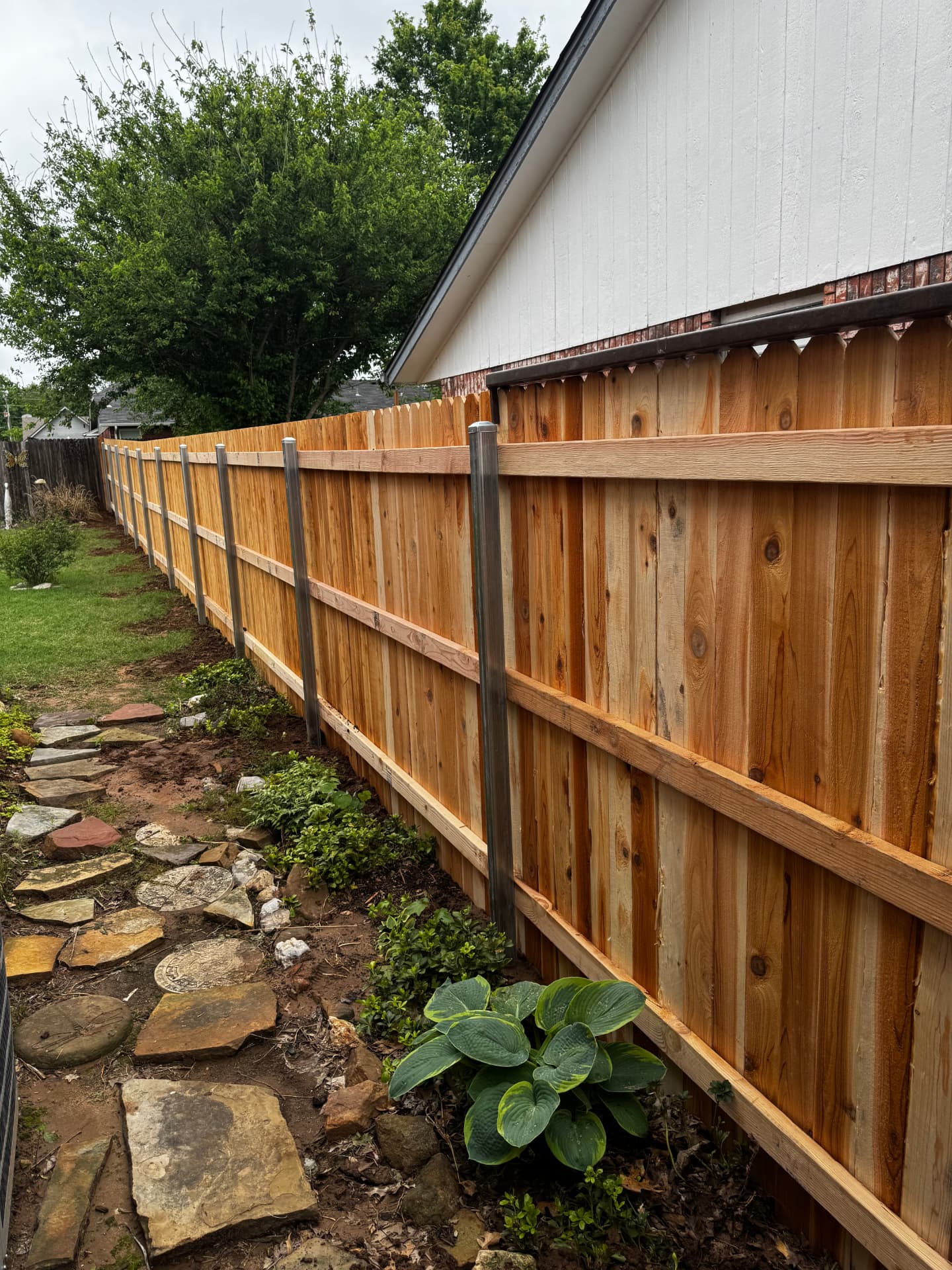 New wood privacy fence with metal posts beside a residential garden path