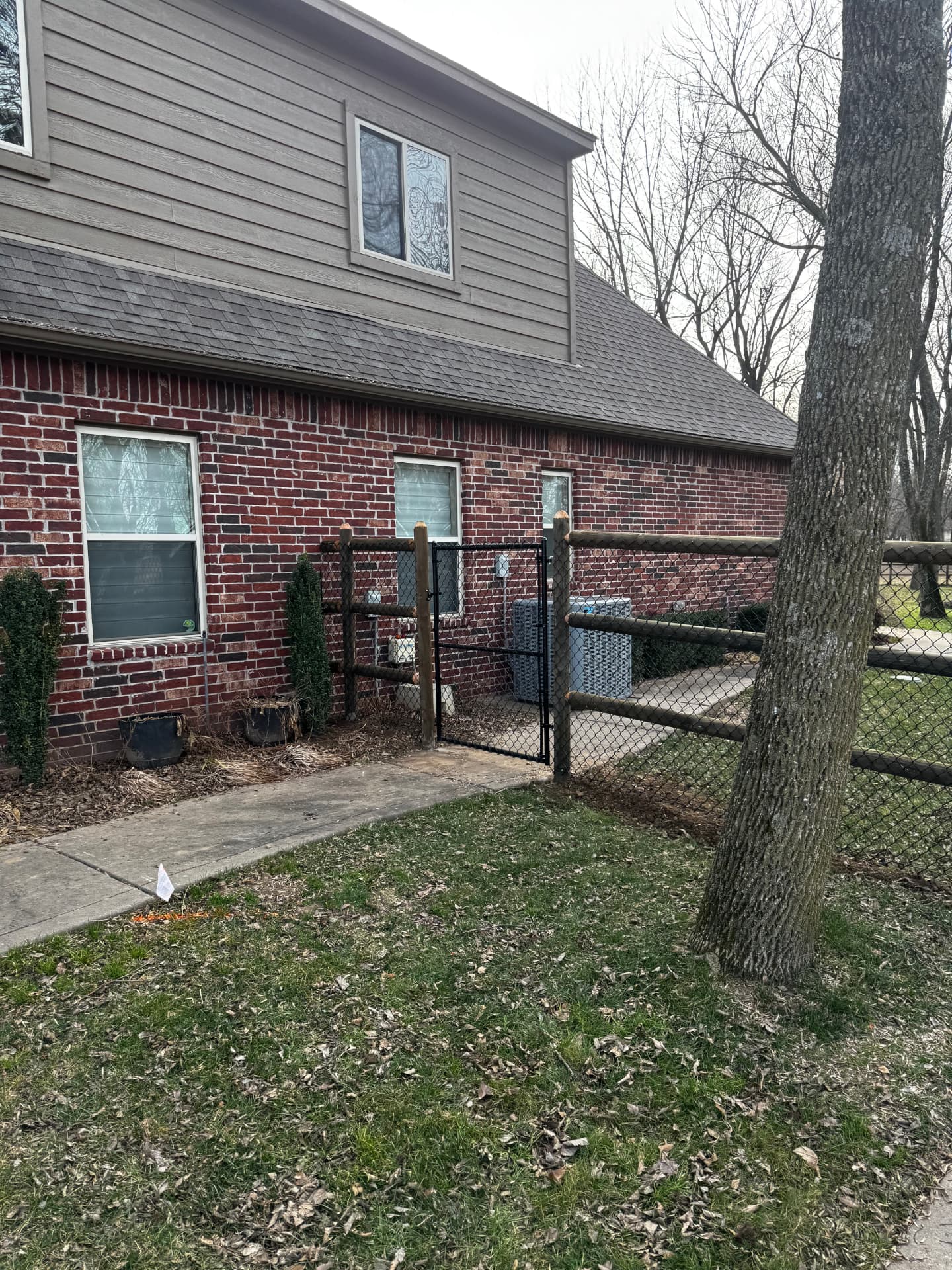 Black chain link gate and mesh added to a round rail fence beside a brick home