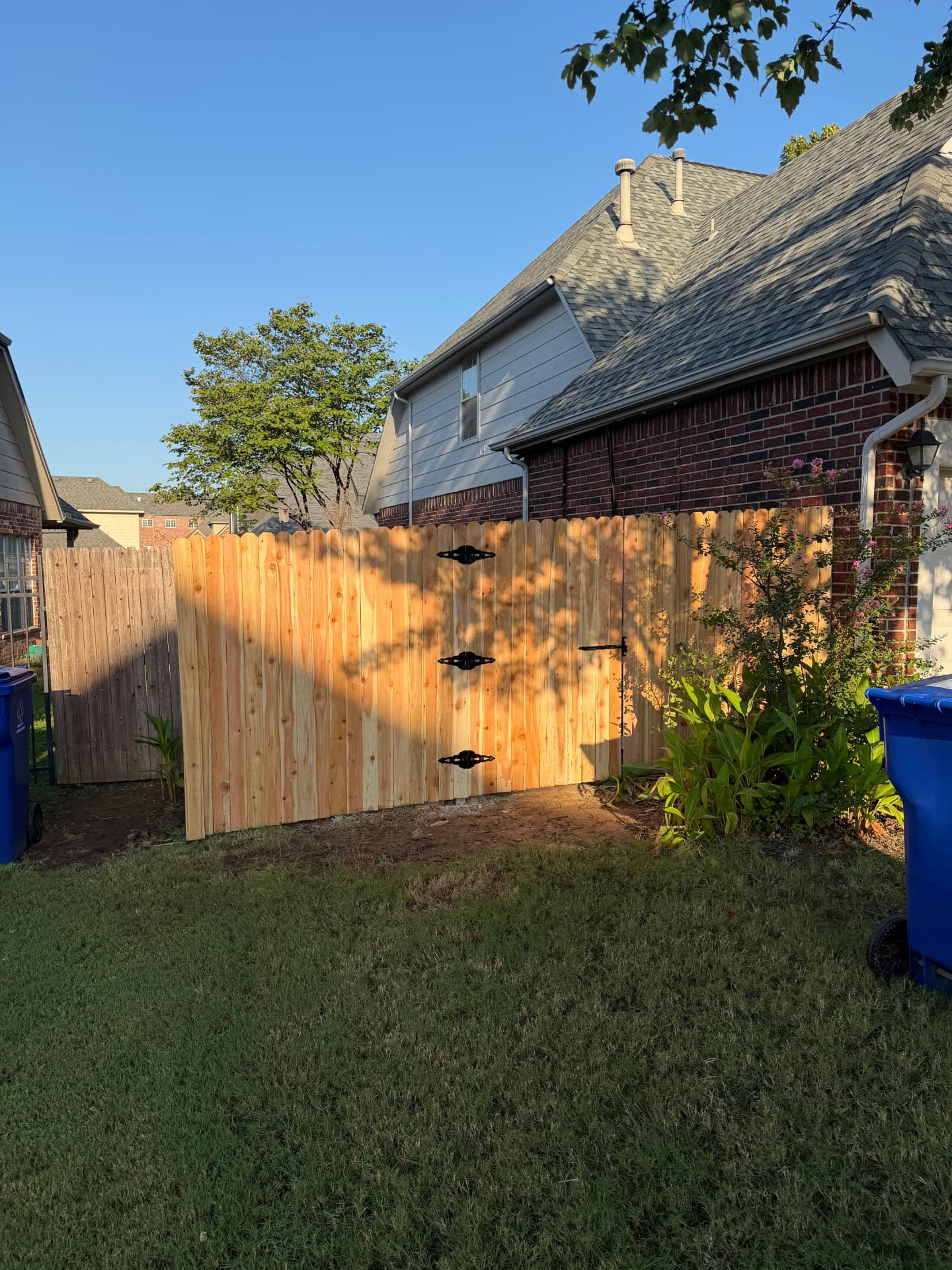New double wood gate with black hinges beside a brick home