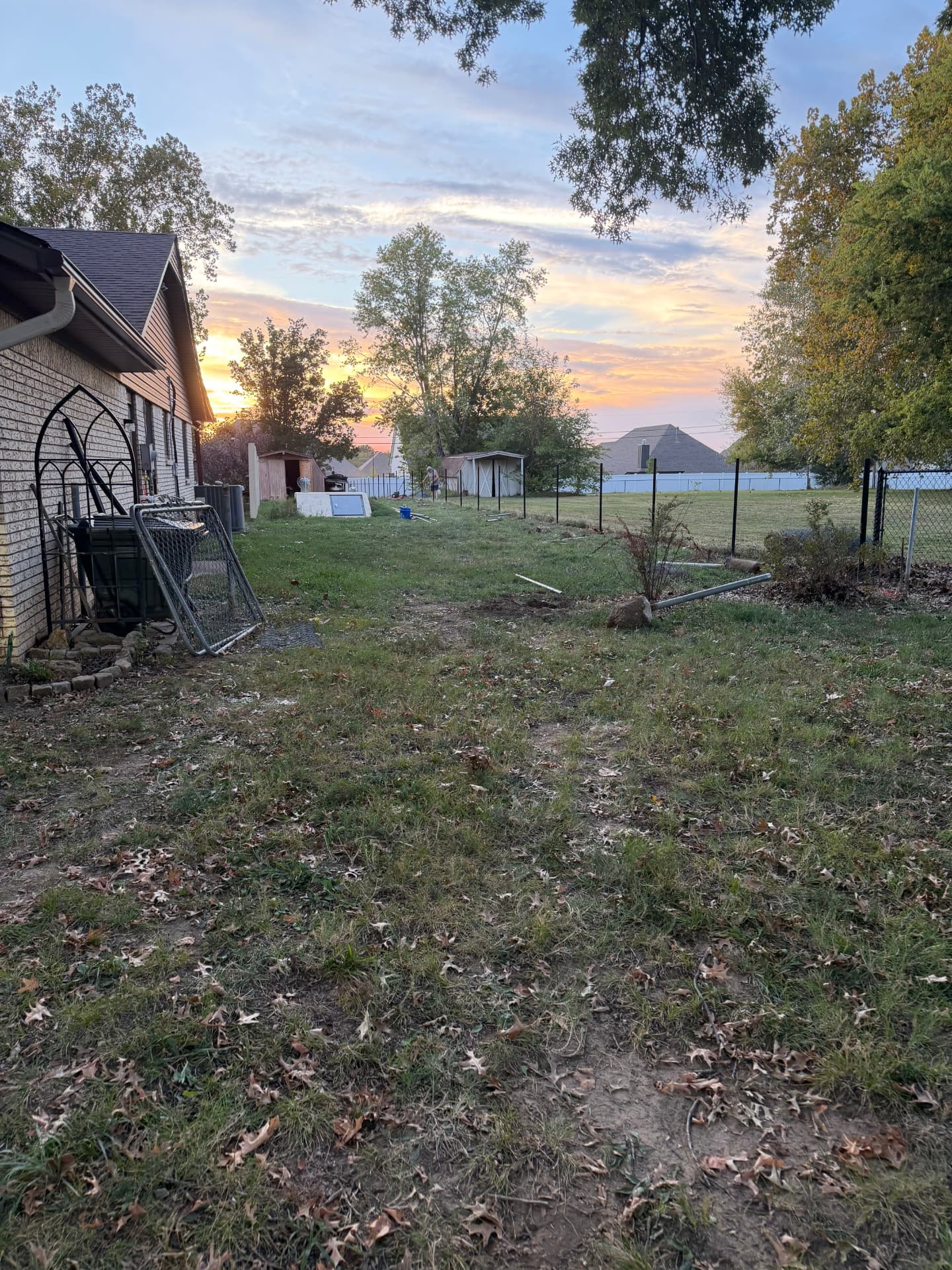 Fence posts and removed chain link panels in a backyard at sunset