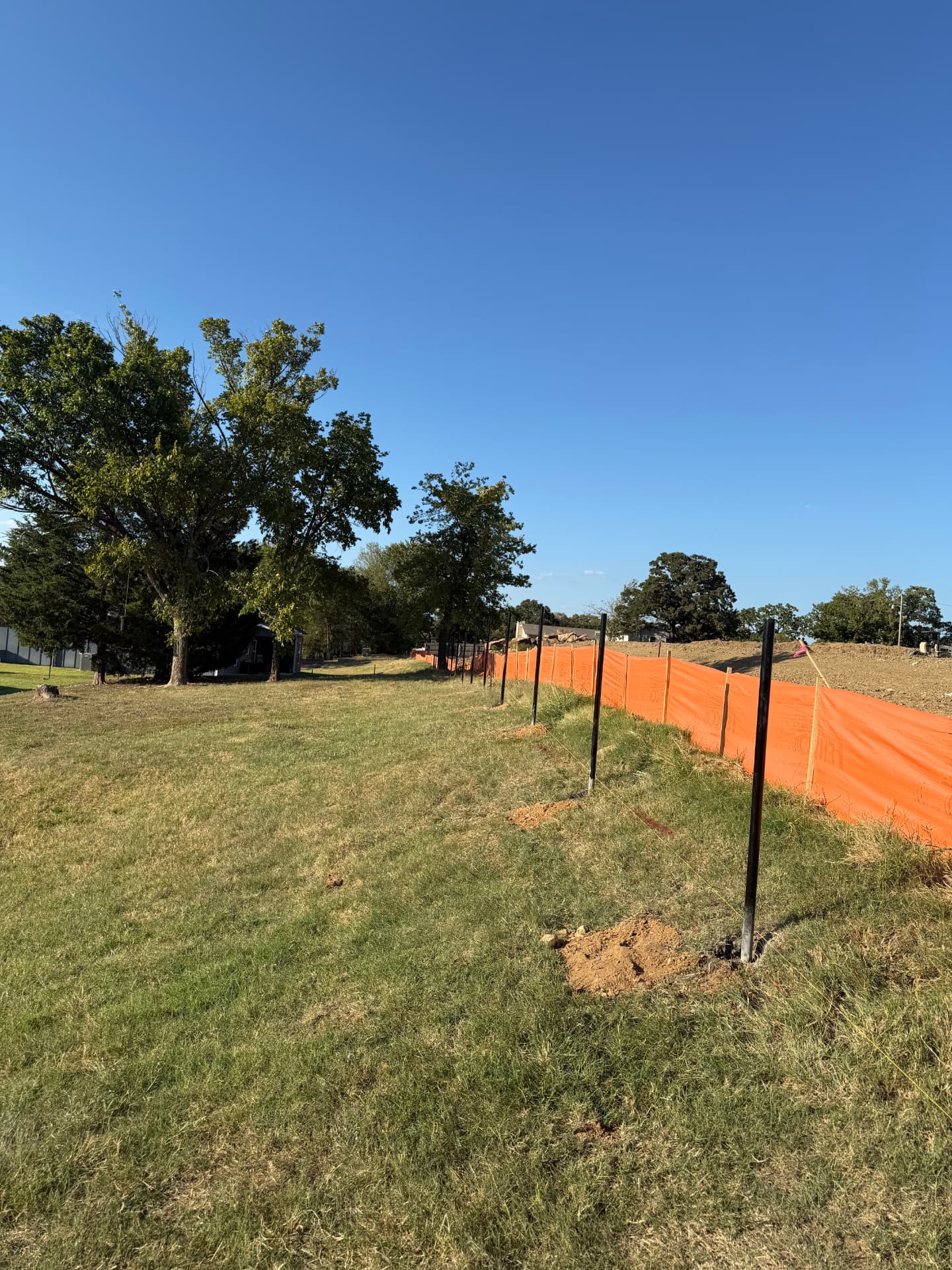 Black fence posts being installed along a grassy property boundary