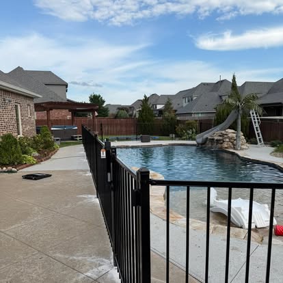 Black metal pool safety fence with a self-closing gate beside a backyard pool