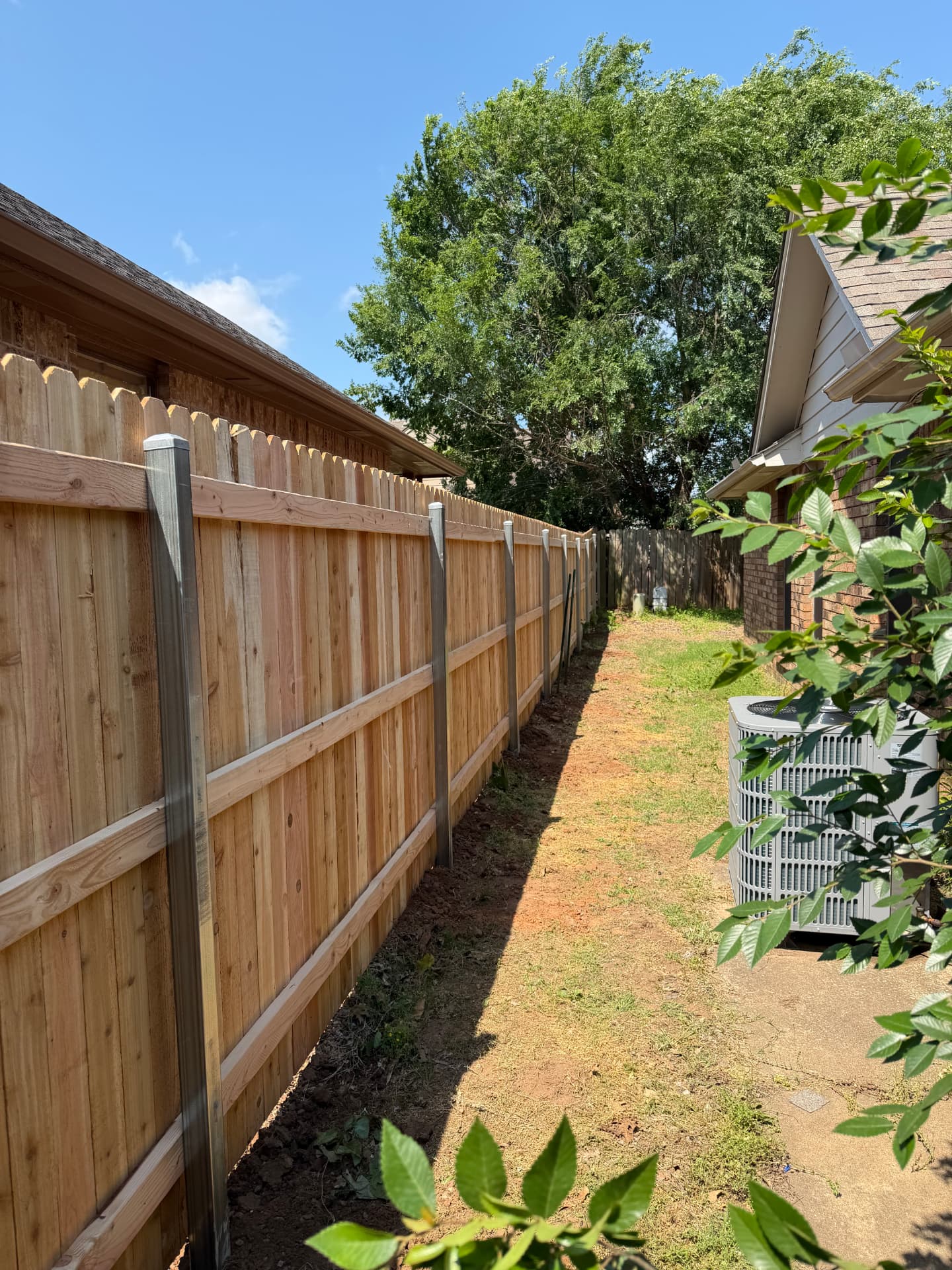 New wood privacy fence with metal posts between two brick homes